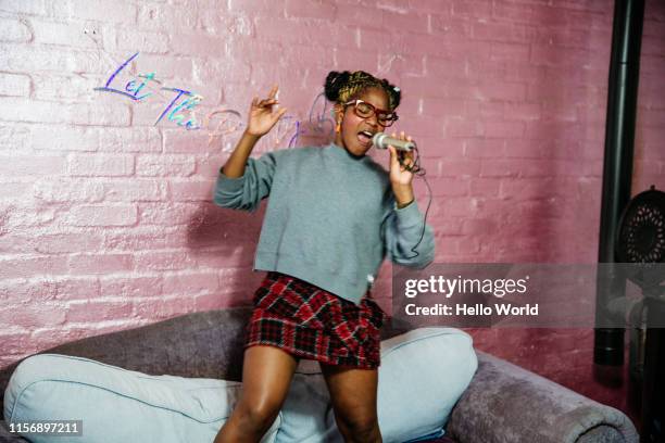 young woman singing with microphone whilst standing on the couch - performer stock-fotos und bilder