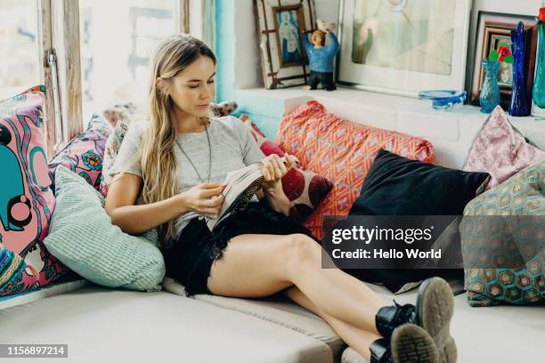 beautiful young woman intently reading on the couch - chill by will 2018 stock pictures, royalty-free photos & images