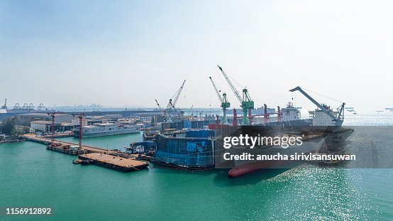 aerial view shipyard have crane machine and container ship in green sea .