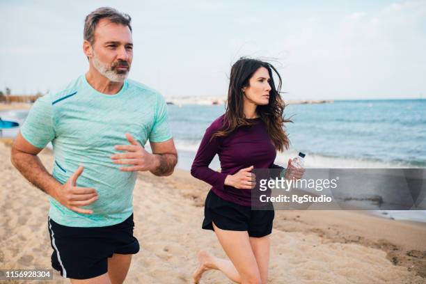 athletic couple jogging on the beach - couple running on beach stock pictures, royalty-free photos & images