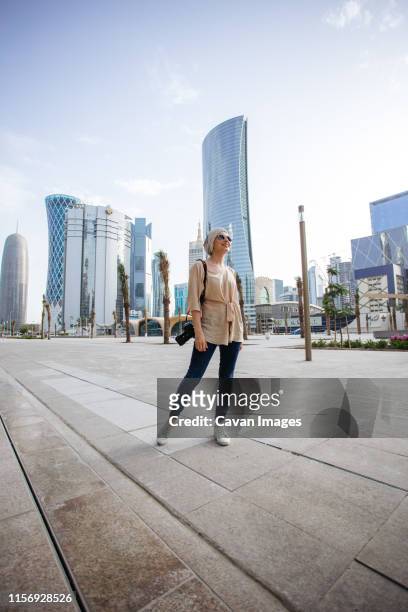 young woman standing in front of skyscrapers in doha - doha street stock pictures, royalty-free photos & images