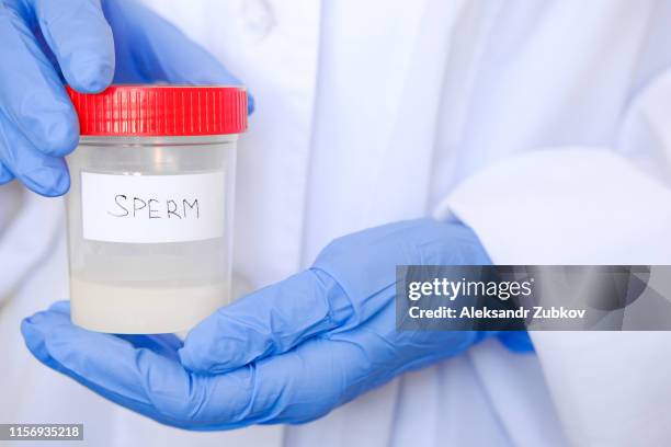 doctor in a white coat and medical gloves holding a container with semen analysis, with the inscription in english. donor sperm for artificial insemination, infertility treatment, planning of children - sperm stock pictures, royalty-free photos & images