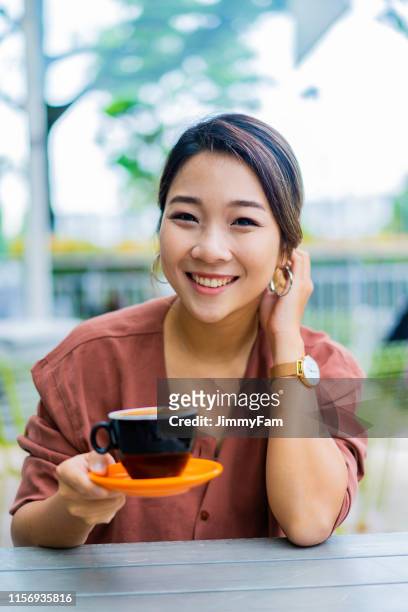 fröhliche asiatische junge frau genießen eine tasse kaffee, während im café sitzen. - china east asia stock-fotos und bilder