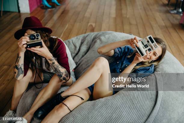 two beautiful girlfriends sitting on beanbags taking snaps of photographer - eccentric hobby stock pictures, royalty-free photos & images