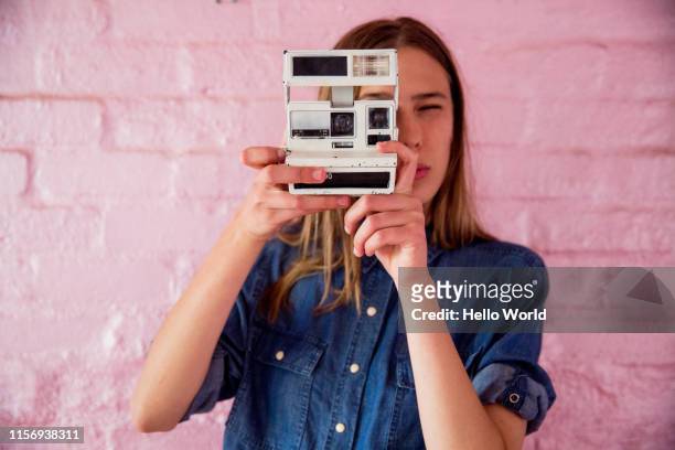 beautiful young woman on pink backdrop taking a photograph with retro camera - mirar fotos - fotografias e filmes do acervo