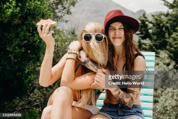 happy oddball girlfriends embrace outdoors with watermelon in hand - frauenpower stock-fotos und bilder