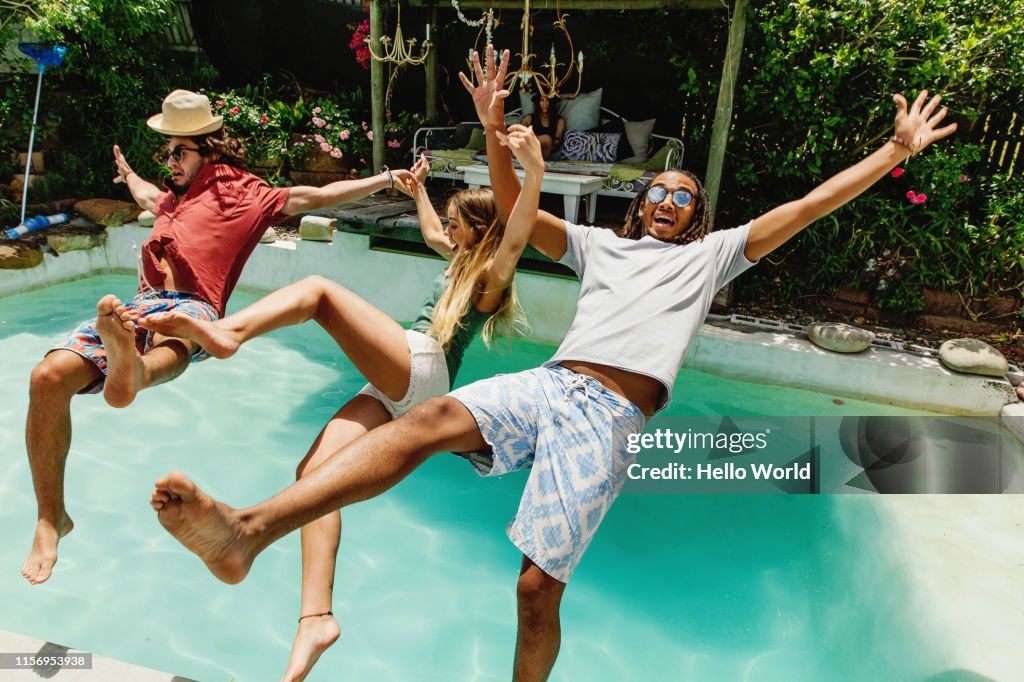 Three fully clothed friends falling backwards into pool
