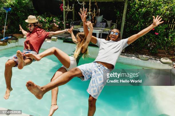 three fully clothed friends falling backwards into pool - fun stockfoto's en -beelden