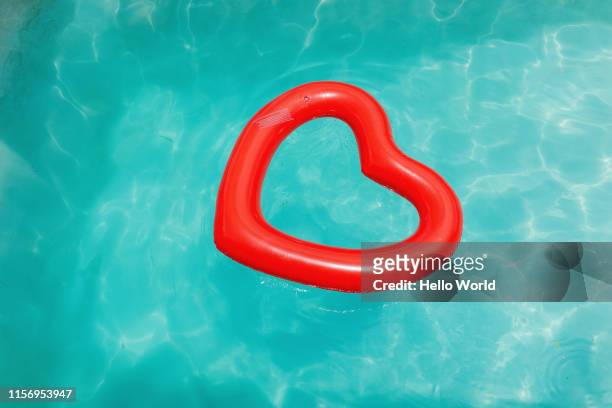 heart-shaped inflatable in crystal clear water - red hot summer party foto e immagini stock