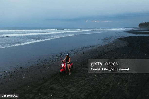 vista aérea panorámica de mujer conduciendo scooter en la playa de arena negra en bali - women black and white motorcycle fotografías e imágenes de stock