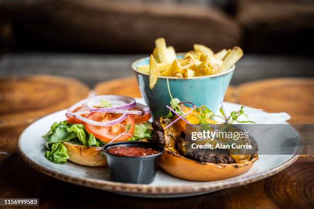 hamburguesa de queso con bollo, patatas fritas y salsa sobre plato circular sobre una superficie de mesa de madera, servida en un pub o restaurante con poca profundidad de campo - burger and chips fotografías e imágenes de stock