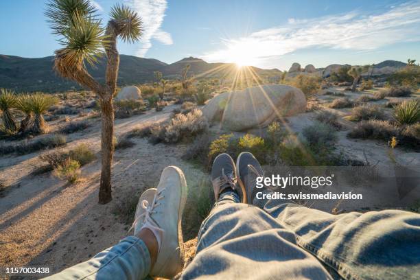 personal perspective of couple relaxing on top of boulder rock at sunrise; feet view;  people travel vacations relaxation concept - joshua tree stock pictures, royalty-free photos & images
