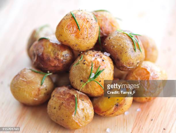 a pile of roasted young potatoes on a wooden table  - roast potatoes stock pictures, royalty-free photos & images
