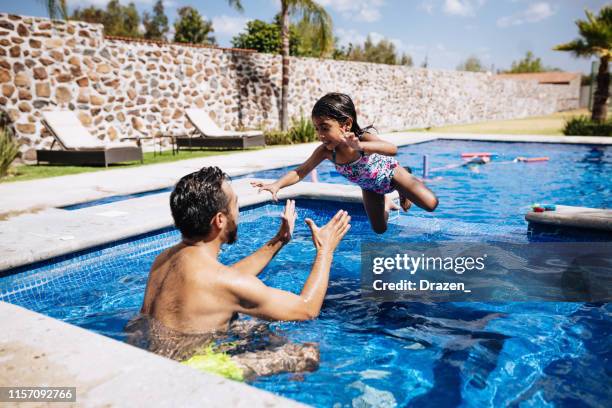 latino father and 4 year old daughter playing in the swimming pool. - young girl jumping into swimming pool stock pictures, royalty-free photos & images