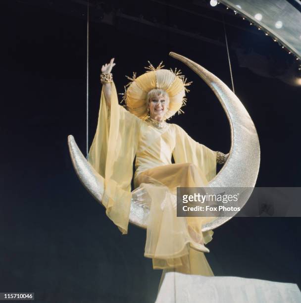 Ginger Rogers , US actress and dancer, in costume as she perches on a crescent moon suspended above the stage during a production of 'Mame', at the...