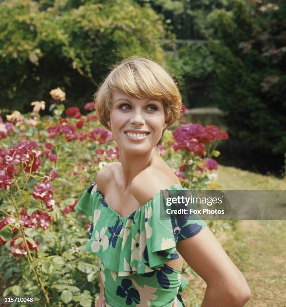 Joanna Lumley, British actress, wearing a floral print dress while posing in a garden at Pinewood Studios during filming of 'The New Avengers', in...