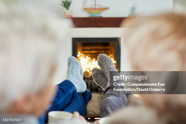 mature lesbian couple with hot drinks on living room sofa at fireside - socks fireplace stock pictures, royalty-free photos & images