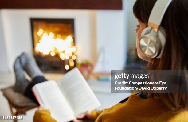 woman with headphones reading in living room - winter relaxation stock pictures, royalty-free photos & images