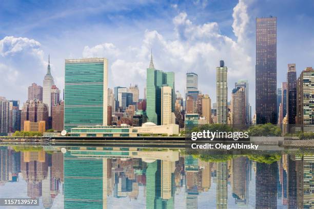 new york city skyline with midtown manhattan skyscrapers, un building and empire state building reflected in water of east river, ny, usa. - east river stock pictures, royalty-free photos & images