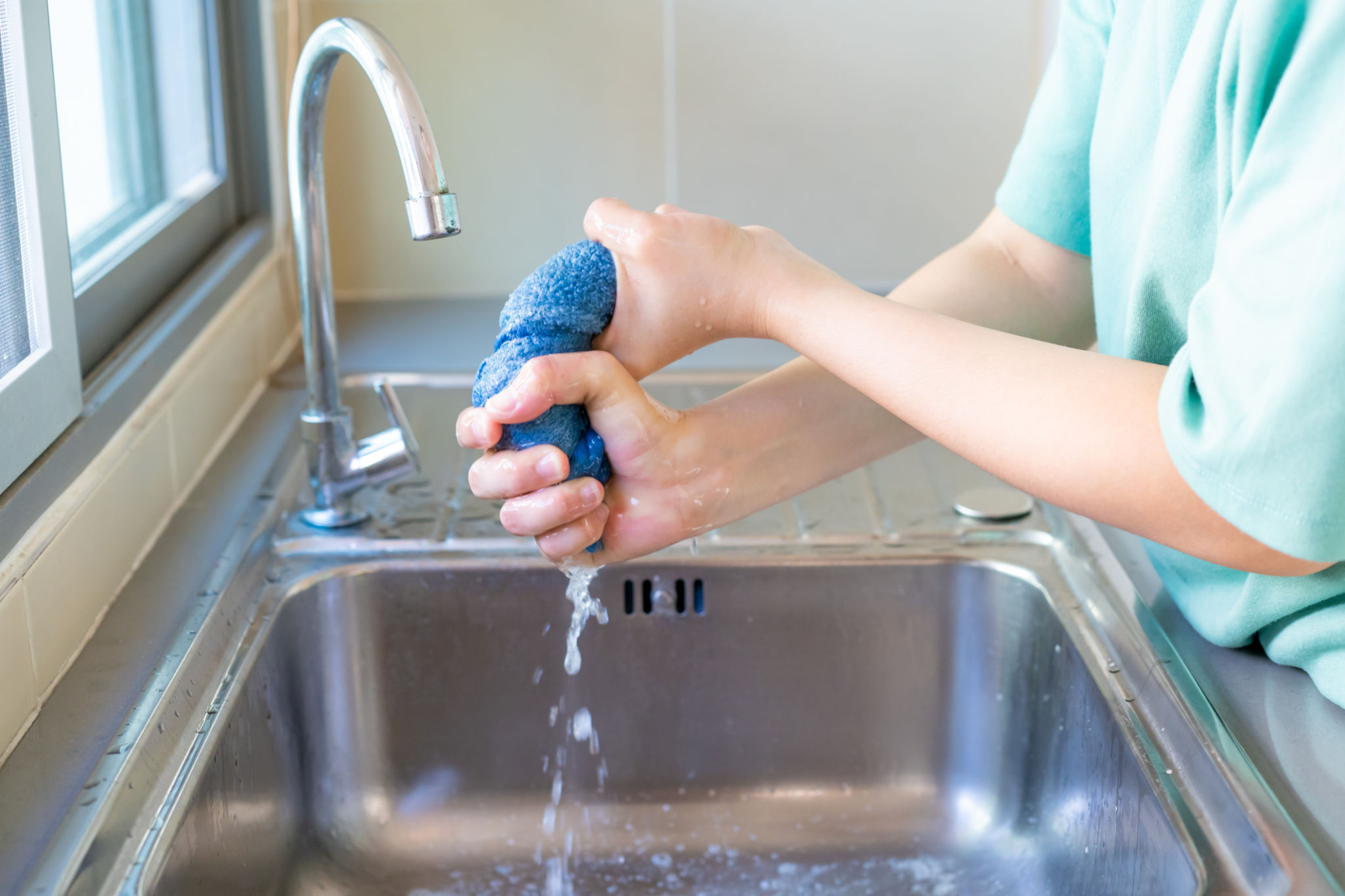 An unrecognizable woman wringing a wet towel in the kitchen sink. An unrecognizable woman wringing a wet towel in the kitchen sink.