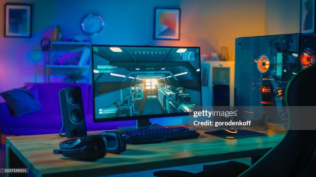 Krachtige personal computer gamer rig met First-person shooter spel op het scherm. Monitor staat op de tafel thuis. Gezellige kamer met modern design is verlicht met warm en neon licht.