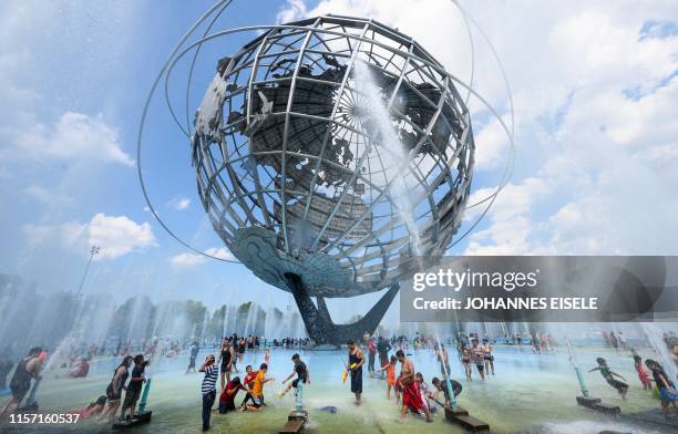 People enjoy refreshing water of a fountain in the Unisphere fountain at Flushing Meadow Corona Park in the borough of Queens on July 21, 2019 in New...
