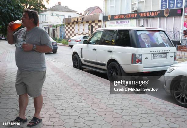 Man drinks beer near a car with poster of Russian President Vladimir Putin and Syrian President Bashar al-Assad, in disputed territory of Crimea,...