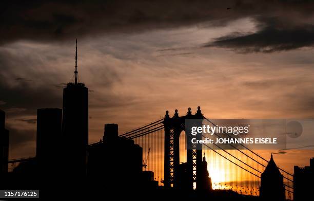 The sun sets behind the skyline of midtown Manhattan and the Manhattan Bridge on July 21, 2019 in New York City. - The United States sweltered in...