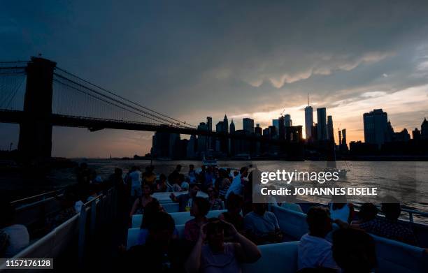 People sit on a ferry while the sun sets behind the skyline of Lower Manhattan on July 21, 2019 in New York City. - The United States sweltered in...