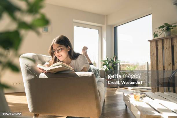 relaxed young woman lying on couch reading a book - reading stock-fotos und bilder