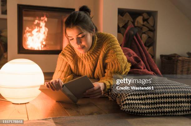 young woman reading book at the fireplace at home - hygge stockfoto's en -beelden