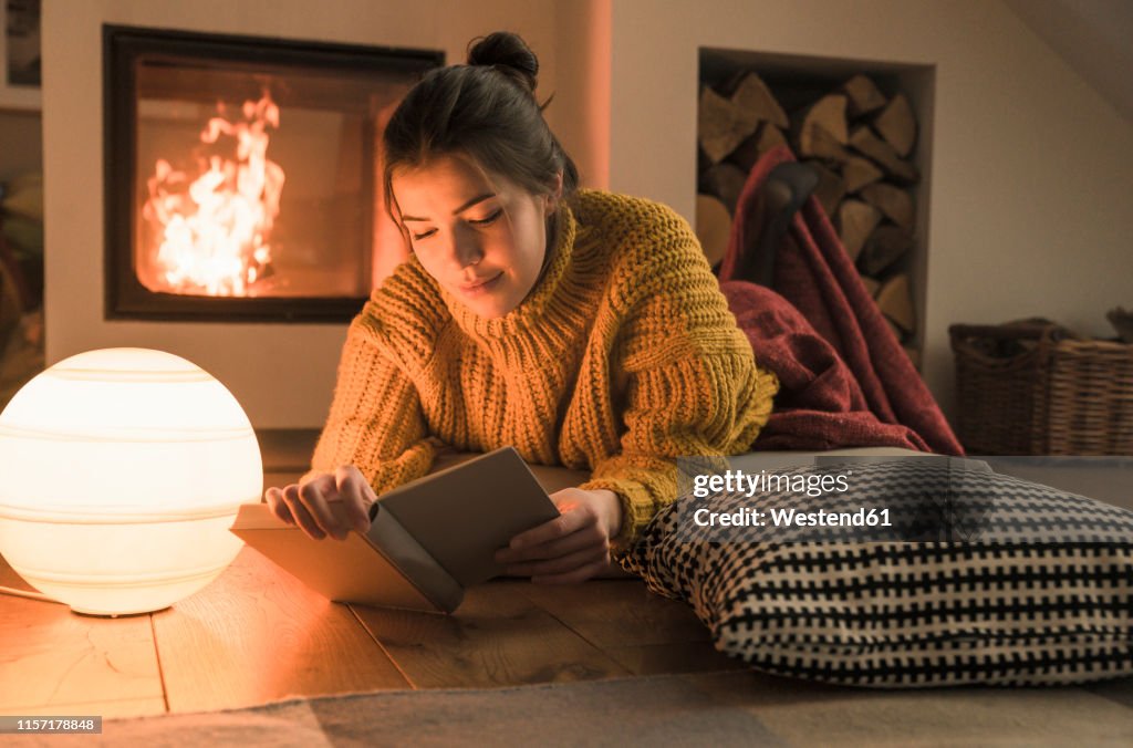 Young woman reading book at the fireplace at home
