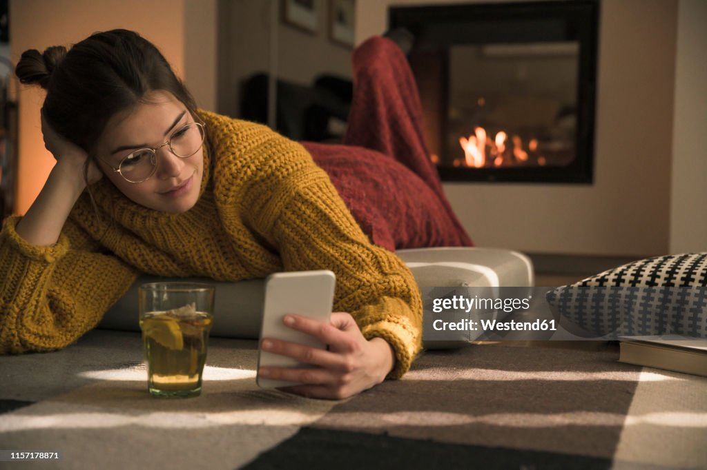 Young woman lying on cushion at home using cell phone