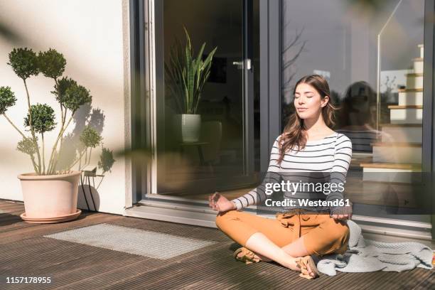 young woman sitting on terrace at home practicing yoga - yoga germany stockfoto's en -beelden