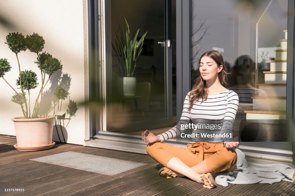 Young woman sitting on terrace at home practicing yoga