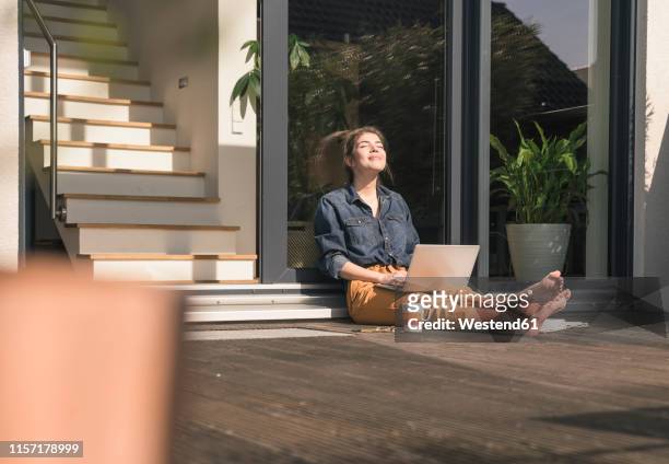 young woman with closed eyes sitting on terrace at home with laptop - work life balance home stock pictures, royalty-free photos & images