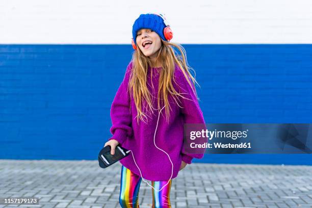 portrait of happy girl singing while listening music with headphones and smartphone - multi colored hat stock pictures, royalty-free photos & images