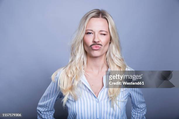 portrait of winking blond woman with fake moustache and hat pouting mouth - barba peluria del viso foto e immagini stock