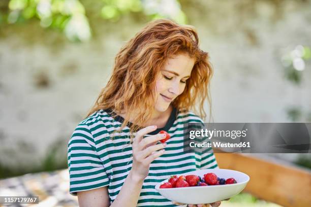 portrait of smiling redheaded young woman with bowl of berries in the garden - eating human flesh stock pictures, royalty-free photos & images