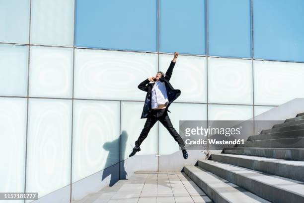 excited businessman on cell phone jumping in the city - business people cheering stock-fotos und bilder