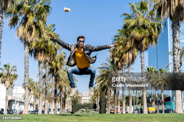spain, barcelona, man in the city jumping in park - mann freudensprung sonne vorderansicht leger stock-fotos und bilder