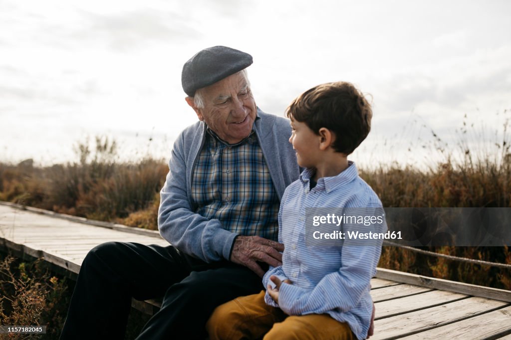 Happy grandfather sitting with his grandson on boardwalk looking at each other