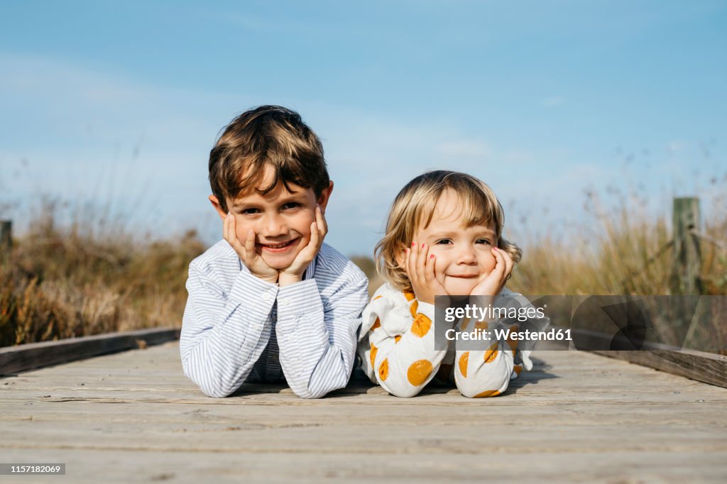 Portrait of boy and his little sister lying side by side on boardwalk