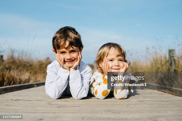 portrait of boy and his little sister lying side by side on boardwalk - schwester stock-fotos und bilder