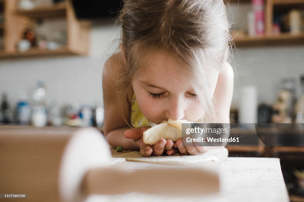 Little girl smelling freshly prepared stuffed pastry