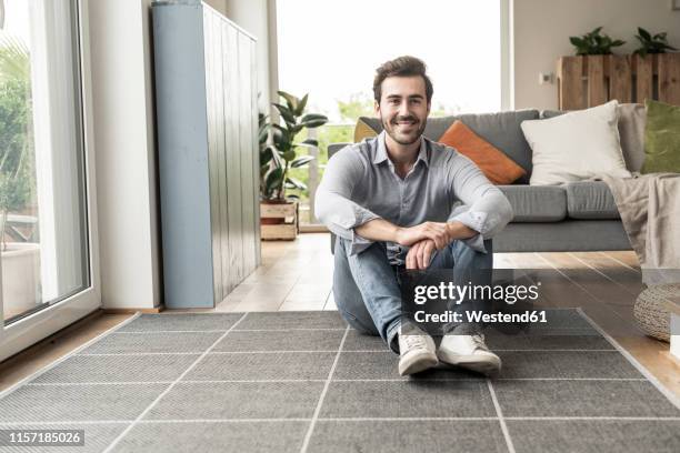 confident young man sitting on floor of his livingroom - sitting on floor stock pictures, royalty-free photos & images