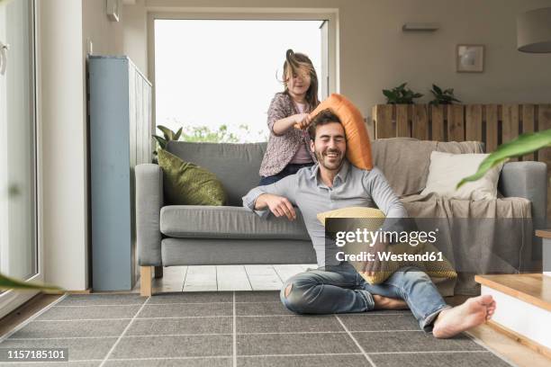 young man and little girl having a pillow fight in the living room - friend mischief stock-fotos und bilder