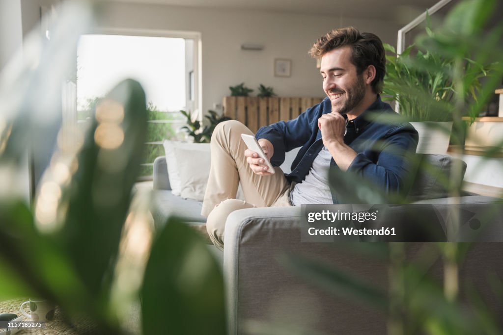 Young man sitting on couch at home, using smartphone