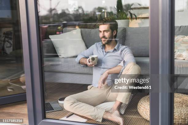 young man sitting in front of window, drinking coffee - coffee window stock pictures, royalty-free photos & images