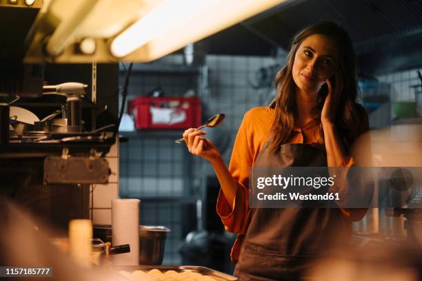 young woman talking on cell phone in restaurant kitchen - preparing food talking stock pictures, royalty-free photos & images